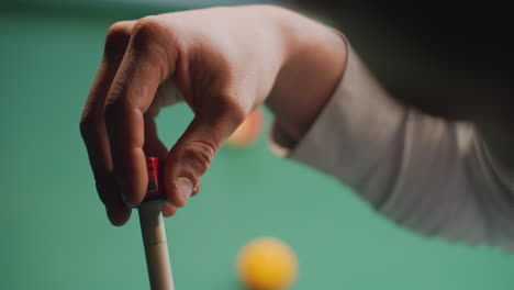 close-up of person's hand chalking cue stick before taking precise shot on green pool table. focus on preparation and technique with blurred billiard balls in background. perfect for sports and gaming