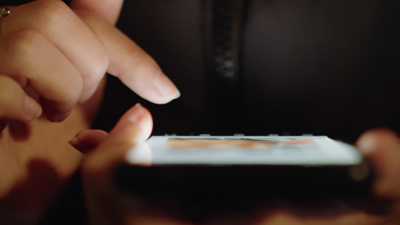 Mani asiatiche che toccano lo schermo illuminato del telefono, primo piano di dita con anelli in penombra, icone di app e feed visibili, gesti delicati di scorrimento e tocco, scenari di shopping e messaggistica, intimo