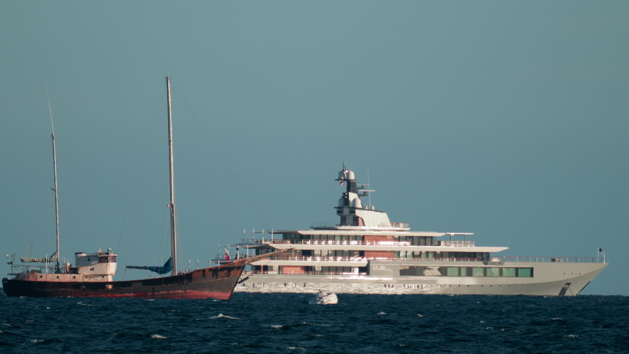 Contrast between a large modern yacht and an old rustic ship floating on blue waves under clear skies