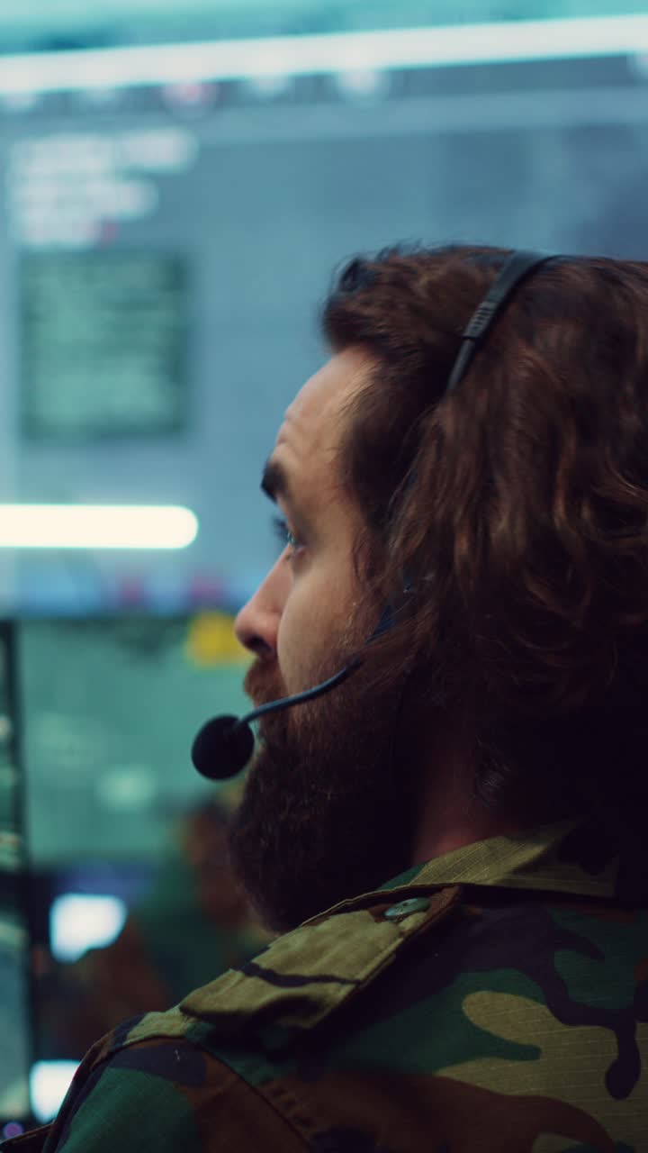 Skjeggete mann i kamuflasjejakke med headset i kontrollrom