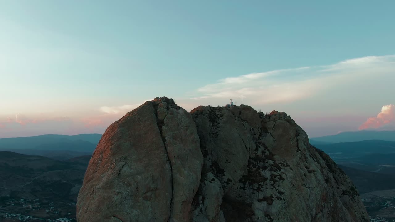 Picco monolitico Peña de Bernal con grandi pareti rocciose fessurate e una croce visibile sulla cima. Ripresa aerea con dolly in