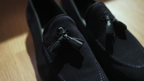 black suede tassel loafers captured in detail on wooden floor with gentle sunlight