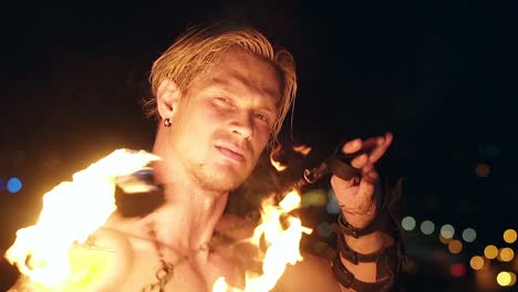 young blond male spins two burning pois looking at camera slow motion shot close-up shot