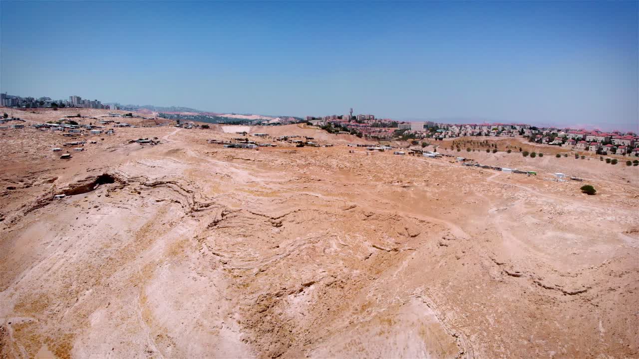 Vista aerea di un paesaggio desertico con insediamenti informali che confinano con una città in lontananza