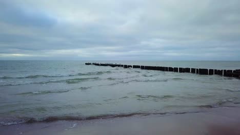 establishing aerial view of baltic sea coast on a overcast day, old wooden pier, white sand beach, low waves crushing against the coast, climate changes, low wide angle drone shot moving forward