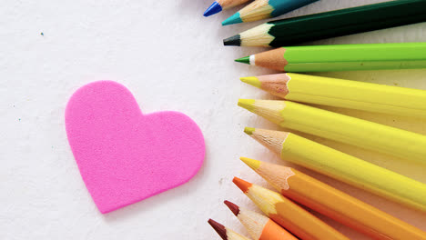 lápices de colores dispuestos en semicírculo con corazón sobre fondo blanco