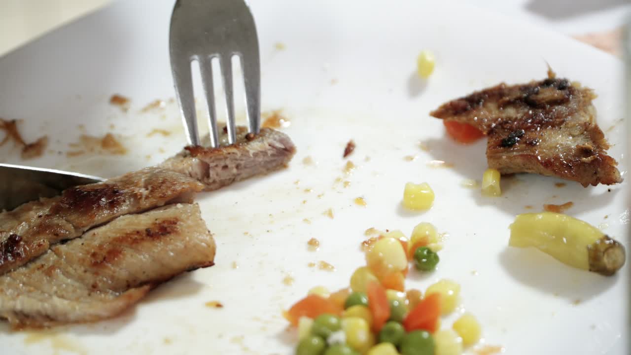 포크와 칼로 긴 고기 스테이크에서 작은 조각을 잘라낸 인간의 손의 클로즈업