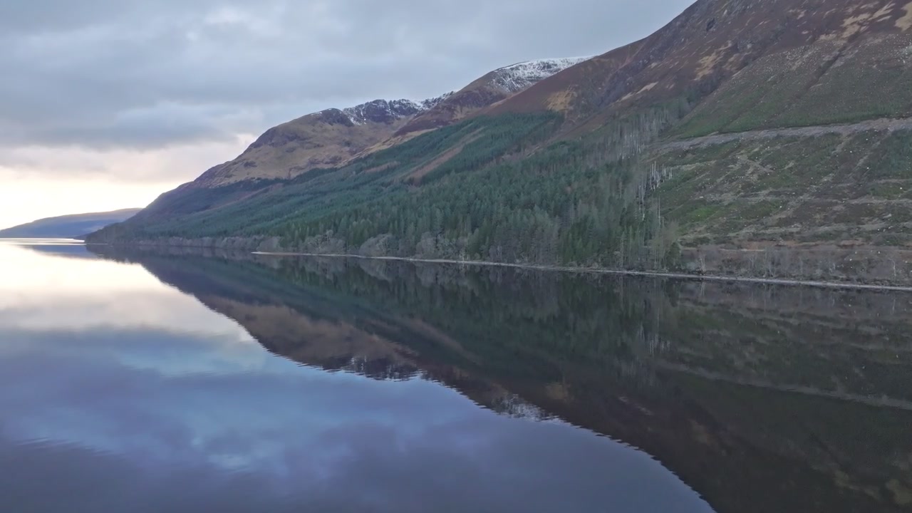 Ripresa aerea cinematografica con drone di un lago solitario (loch scozzese) circondato da montagne e foresta.