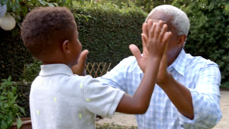 young black boy playing clapping game with grandad in garden