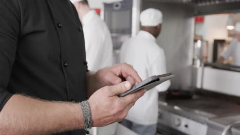 caucasian male chef using tablet in kitchen, slow motion