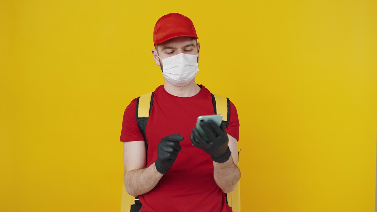 Male courier wearing protective face mask using smartphone and showing device with green chroma key screen