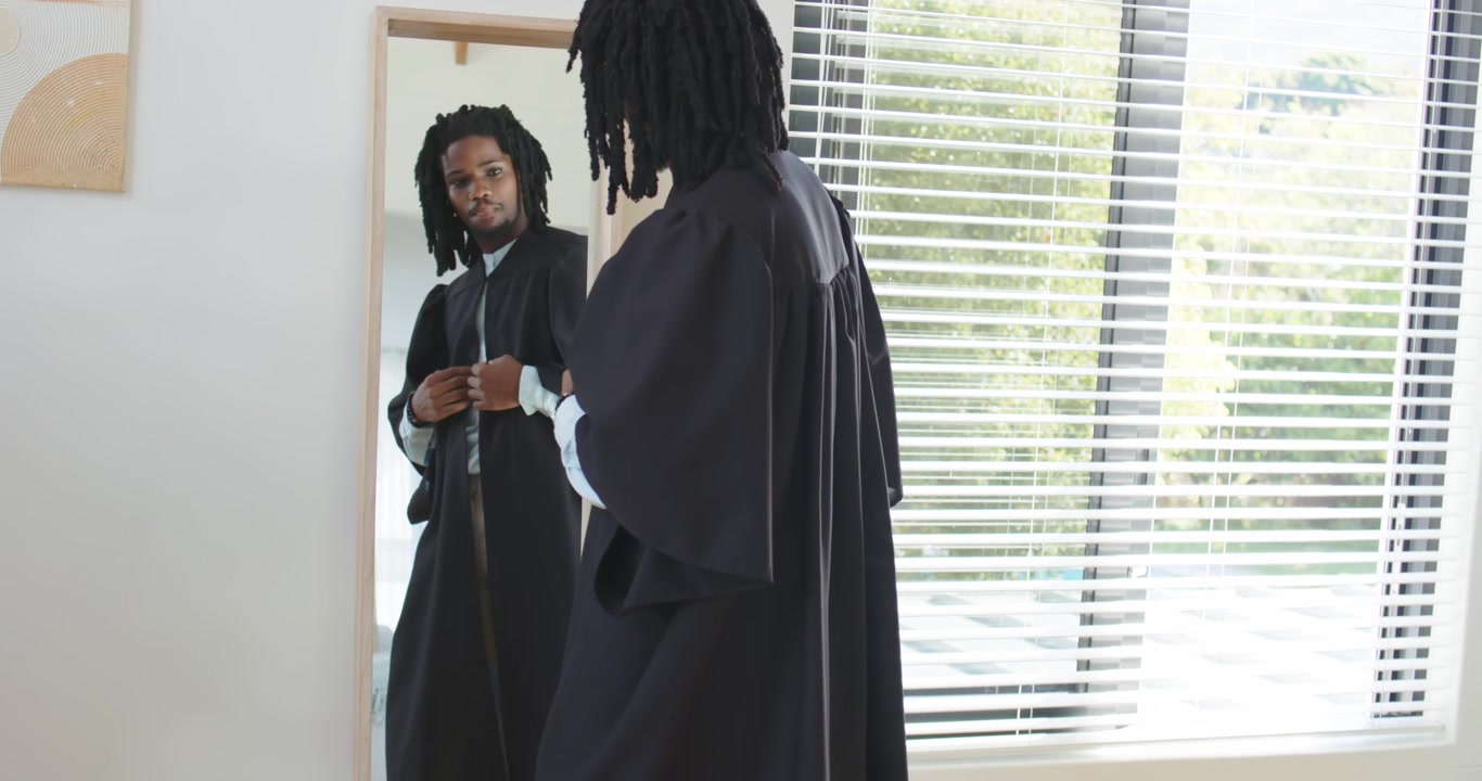 Uomo afroamericano che allaccia e liscia una veste cerimoniale nello specchio della camera da letto, preparandosi per un evento