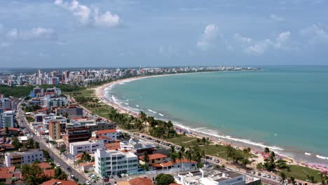 trucking left aerial shot of the tropical intermares beach in cabedelo, brazil near joao pessoa with apartments, homes, and palm trees along the coastline in the state of paraiba on a warm summer day