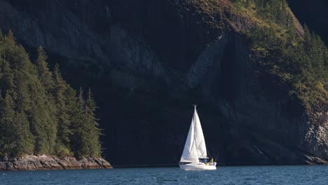 Sailboat-by-Steep-Cliffs-of-Alaskan-Coastline-Sailing-on-Calm-Water-on-Sunny-Day-Slow-Motion-Wide-View