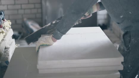 repairman holds saw and starts cutting gypsum board on table