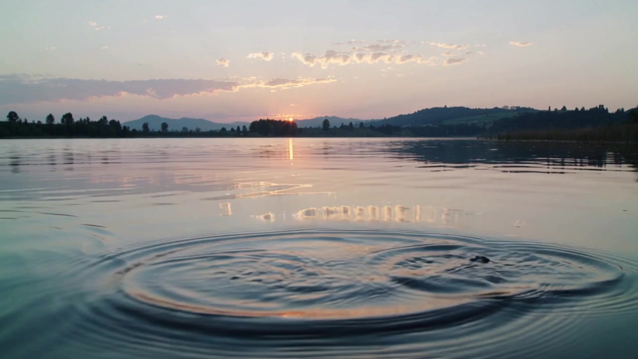 Superficie del lago increspata che forma increspature concentriche dopo un piccolo spruzzo al tramonto, con il riflesso del sole.
