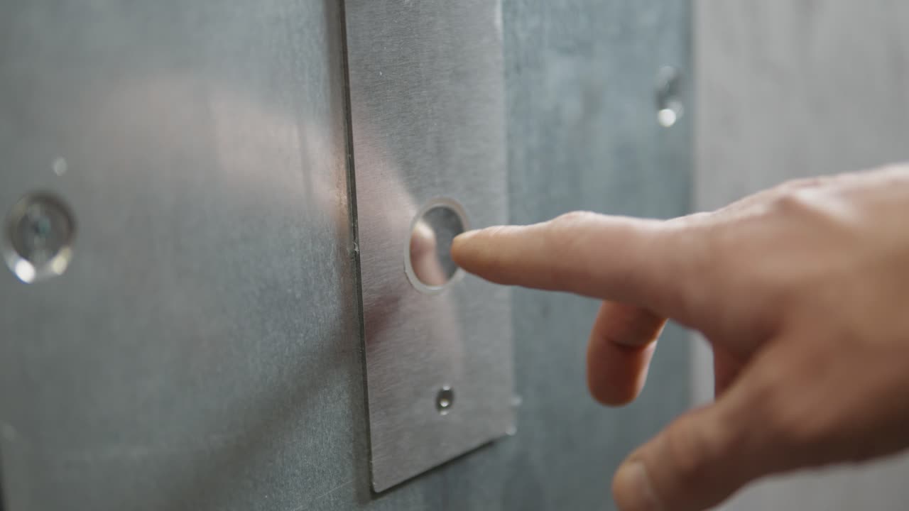 A button on a shiny minimalistic steel panel is being pressed.
