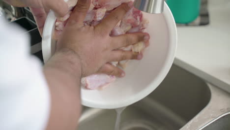 man rinsing and emptying water from a bowl of raw chicken