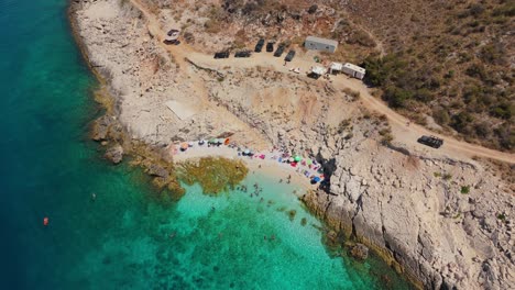 una playa oculta en albania con aguas turquesas y unos pocos visitantes en un día soleado, vista aérea