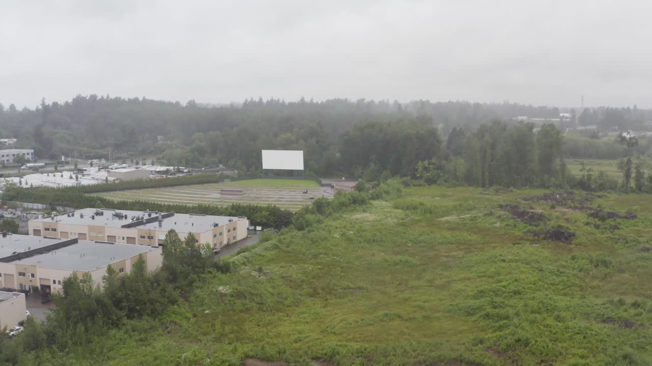Aerial over marshland adjacent to commercial industry drivein and lush green pastures of forests on a hot cloud covered rainy day