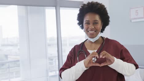 Portrait-of-happy-african-american-female-doctor-with-face-mask-in-hospital-room,-slow-motion