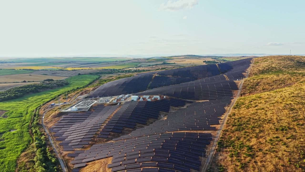 Solcellepark spredt ud over bølgende bakker med flere rækker solpaneler under en klar himmel