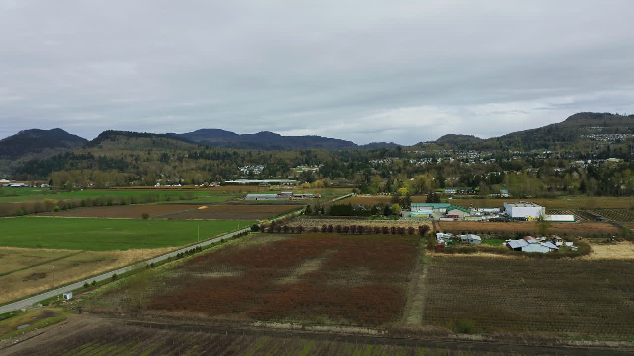 filas en el campo de la granja con el edificio distante bajo cielos nublados cerca de las estribaciones de las montañas