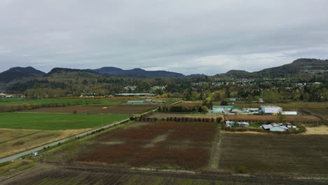 Filas-En-El-Campo-Agrícola-Con-Un-Edificio-Distante-Bajo-Un-Cielo-Nublado-Cerca-De-Las-Estribaciones-De-Las-Montañas