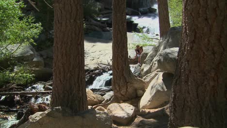 a mother and daughter enjoy a quiet moment beside a waterfall in a beautiful forest