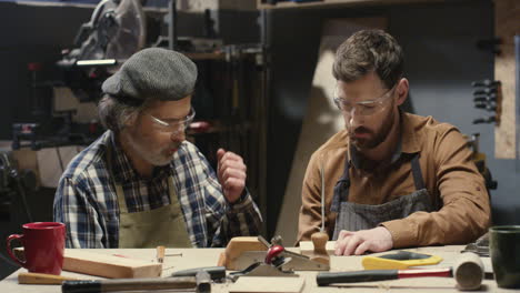 old father carpenter teaching his young son to process and work with timber in workshop