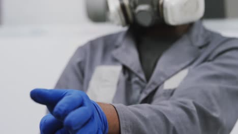 african american male car mechanic wearing a face mask and putting on protective gloves