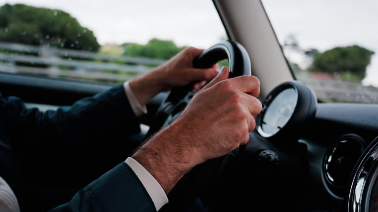 Close up of a man's hands on a steering wheel, driving a car on the road