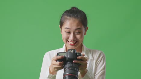 close up of asian photographer looking at the pictures in the camera then screaming goal celebrating satisfied with the result while standing on green screen background in the studio