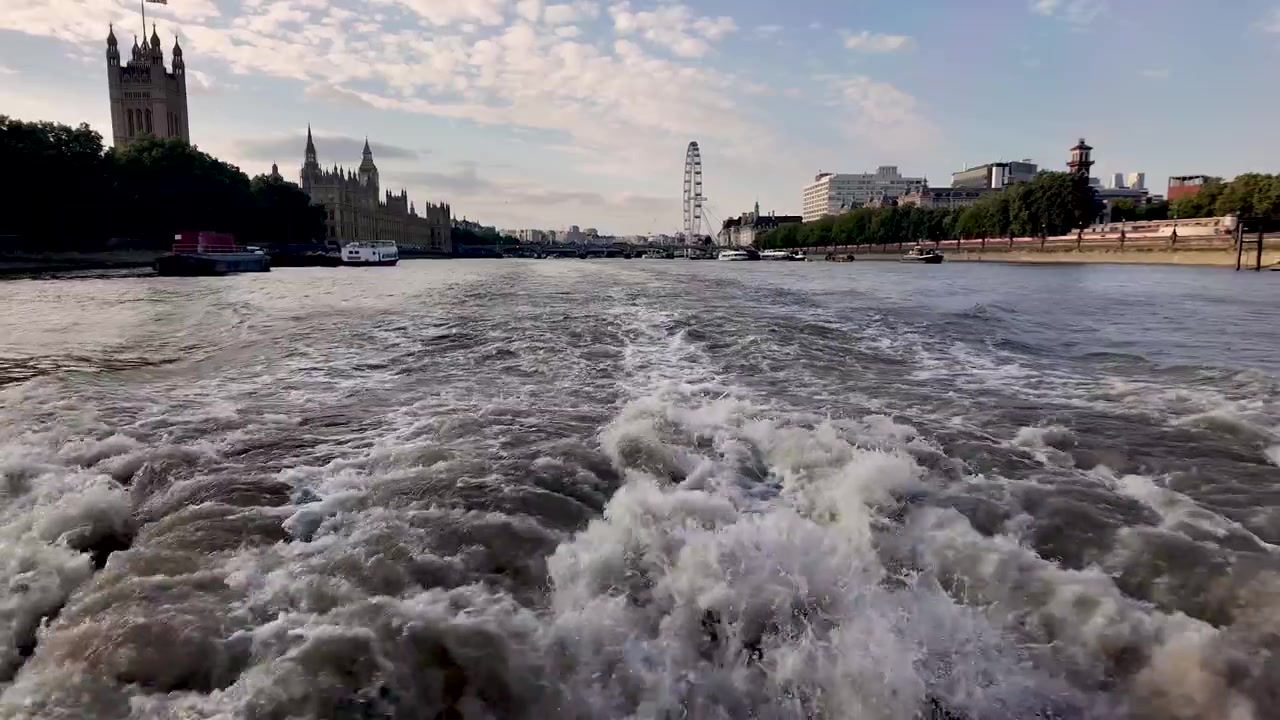 Skummende kjølvann etterlater seg en rask passasjerbåt på Themsen nær Westminster Pier, med Westminsterpalasset og London Eye foran