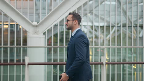 French-businessman-walks-casually-along-modern-building-holding-journal-and-phone-with-good-vibe