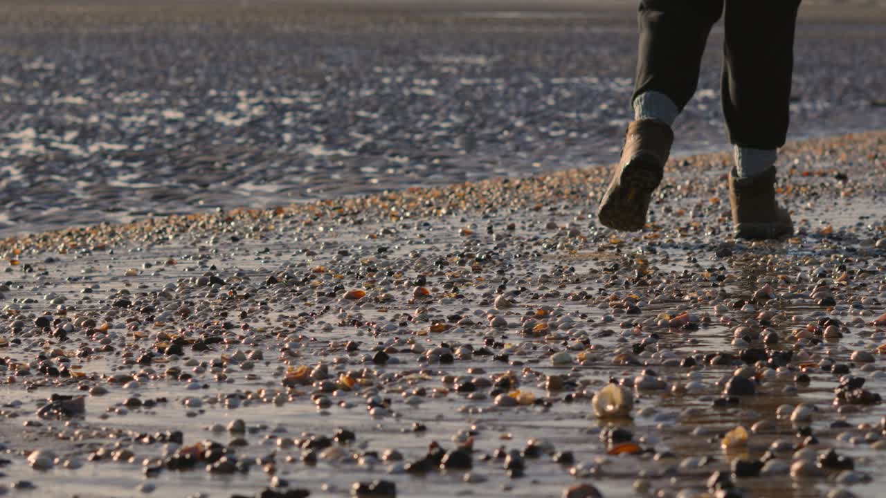 Female Hiker Feet Taking Leisure Walk Along SeaShell Beach in Winter in Slow Motion as Camera Gently Pans Up 4K