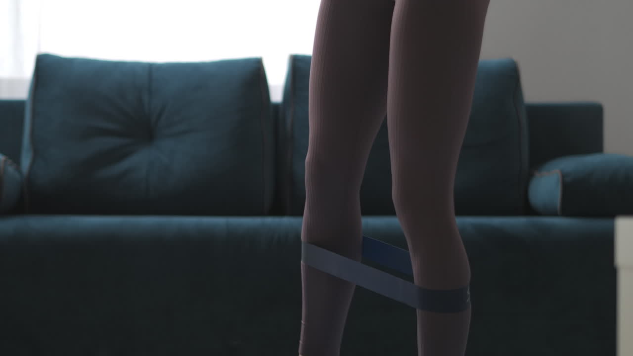 панорама женского тела во время тренировки с помощью фитнес-эластичной полосы напрягает мышцы ног для потери веса и хорошей формы домашняя тренировка