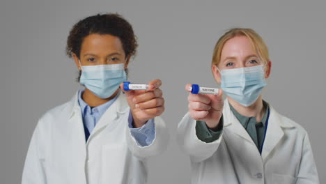 fotografía de estudio de trabajadores de investigación de laboratorio con máscaras faciales sosteniendo tubos de ensayo etiquetados con covid-19 y vacuna