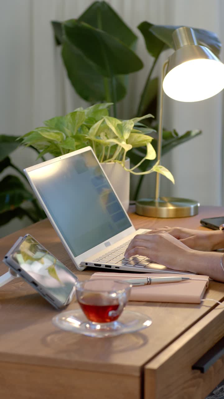 Vertical video: Female hands positioning on laptop, typing steadily to finish task at home desk