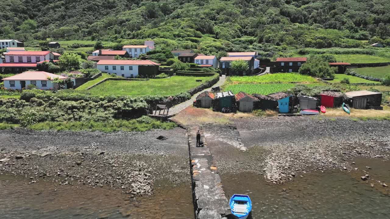 Drone che avanza rapidamente sopra un viaggiatore su un pontile verso la costa alla Caldeira do Santo Cristo, Isola di São Jorge, Azzorre, Portogallo