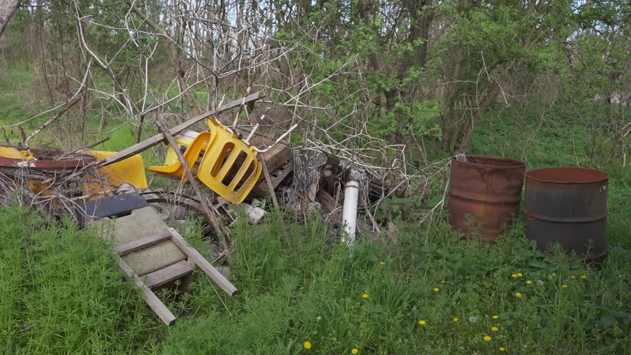 Discarded items and rusted barrels in a rural overgrown junkyard