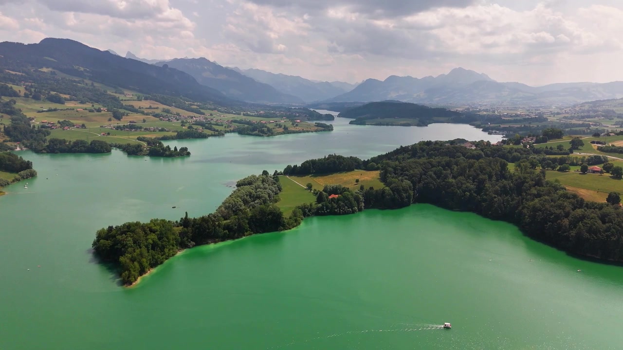 Lago di Greyerz vicino a Pont-la-Ville, Friburgo, Svizzera, che rivela penisole boscose, un bacino idrico turchese, campi ondulati, barche sparse e le Prealpi friburghesi, ripresa orbitale con drone