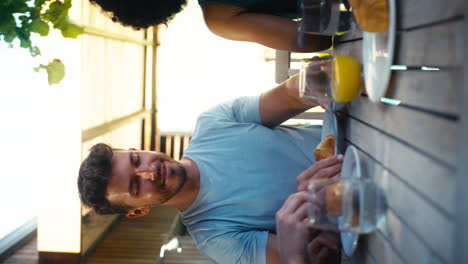 Vertical-Video-Of-Smiling-Multi-Cultural-Friends-Eating-Breakfast-Outdoors-At-Home-Together