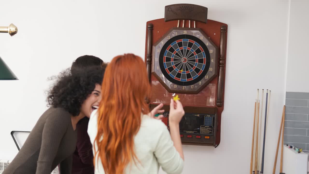 Cheerful woman playing game of dart with friends at home