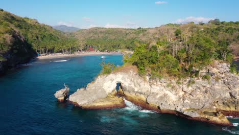 cinematic aerial video of tropical island with turquoise water waves crushing rocky cliffs, arch, boats, coastline, crystal bay beach, nusa penida, bali, indonesia, aerial view