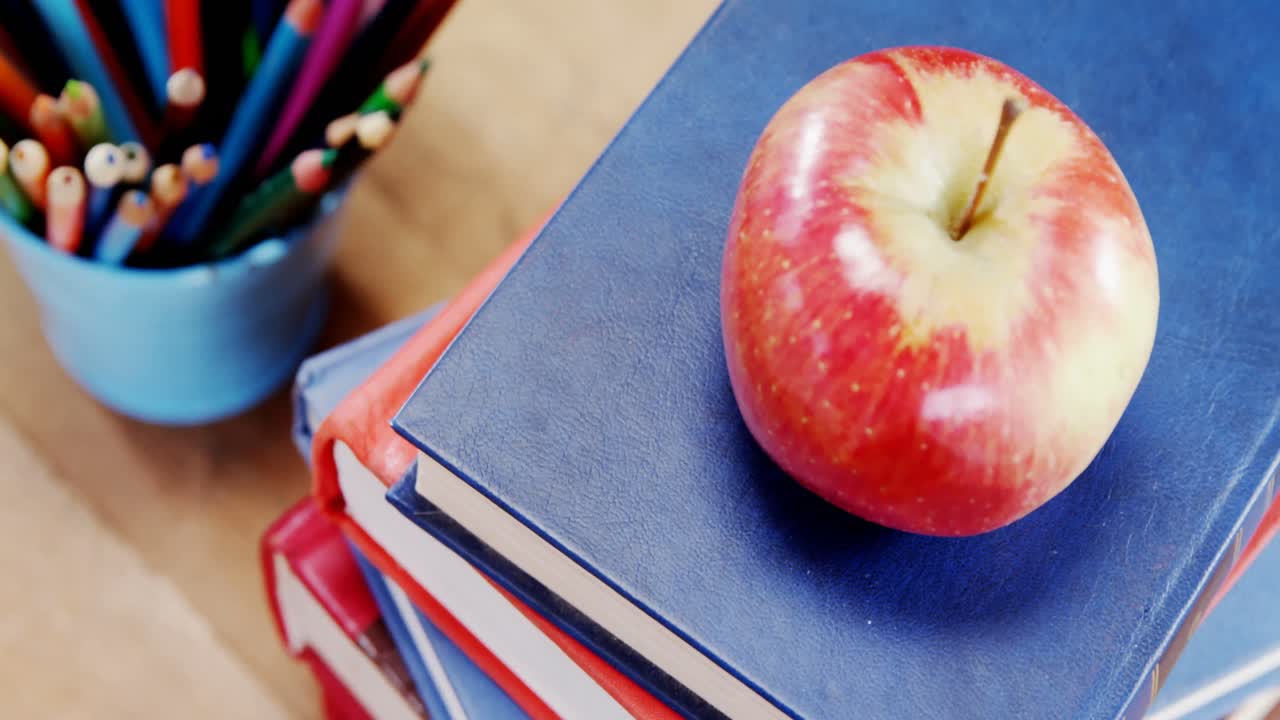 manzana en una pila de libros con un soporte de lápiz en la mesa
