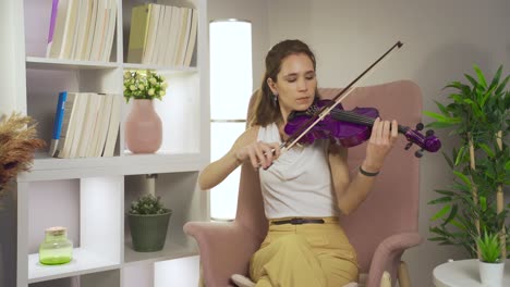músico talentoso mujer tocando el violín sentado en el sofá en casa.