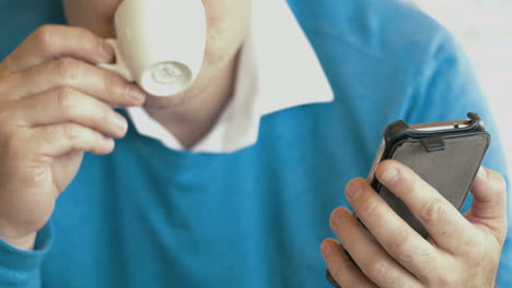 hombre adulto usando un teléfono inteligente y bebiendo café