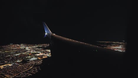 plane landing in an airport next to a city at night from the inside looking outside at the wing