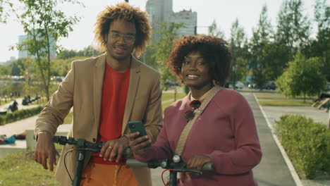 portrait of happy african american friends with e-scooters and smartphone